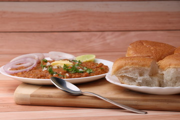 Pav Bhaji is a fast food dish from India, Thick and spicy vegetable curry, fried and served with a soft bread roll/Bun Paav and butter. Served over colourful or wooden background