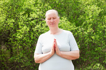 Naklejka na ściany i meble A beautiful adult woman, wearing a white t-shirt, meditates with folded arms. Recreation. Healthy life concept.