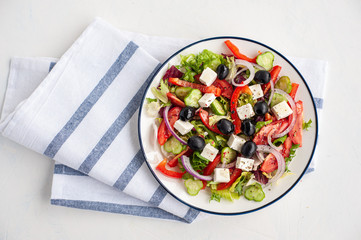 Vegetable salad with olives and feta cheese. Greek salad in a plate on a white concrete background. Copy space.
