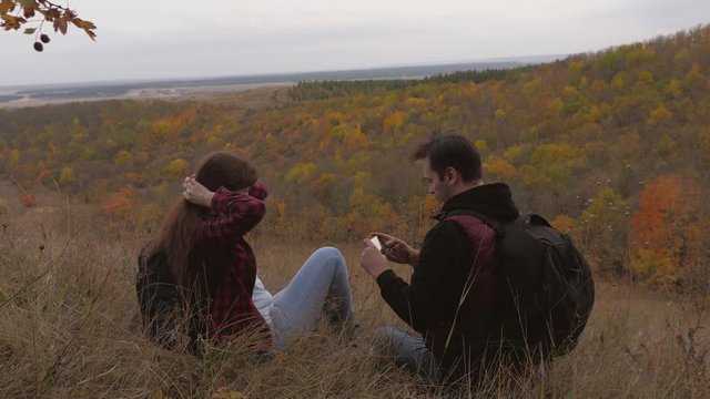 travelers are photographed on smartphone against backdrop of beautiful autumn landscape. Free travelers man and woman with backpacks take selfie while relaxing. teamwork of travelers. travel concept