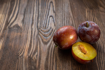 Juicy, ripe, delicious plums on a wooden table, background under a tree