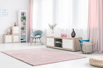 Spacious living room interior with wooden cabinet, grey elegant chair and fluffy pastel pink rug