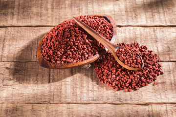 Annatto seeds in bowl on wooden background - Bixa Orellana.