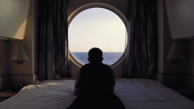 Man lays on bed in front of the window in stateroom onboard cruise ship