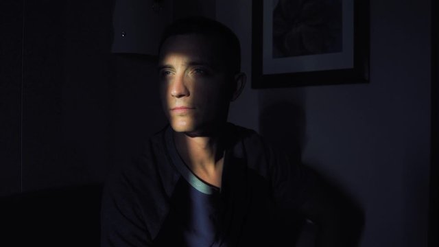 Young man face with sunbeam on eye in dark black room