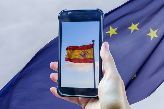 Spain flag in a smartphone display in front of a european union flag.