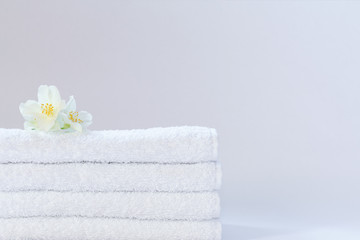 Four white neatly folded terry towels with a jasmine flower on a light background.