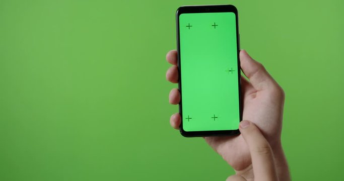 Hands of man holding a phone with vertical green chroma key screen. isolated on green background, swiping the touchscreen 4k template