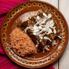 Mexican chicken enchiladas with mole sauce and rice on white background