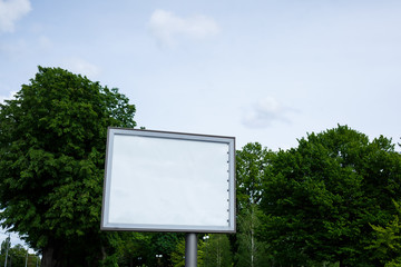 A large metal billboard on the street with a place for your advertising, a billboard on a background of trees