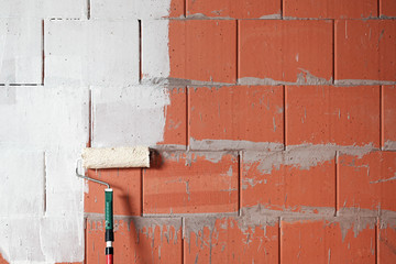 Painting a brick wall white with a paint roller on a construction site, background concept for renovation, building and home, copy space