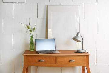 Small vintage table of reddish wood with laptop, desk lamp and a picture frame in front of a raw white wall, tiny home office place in the living room, copy space