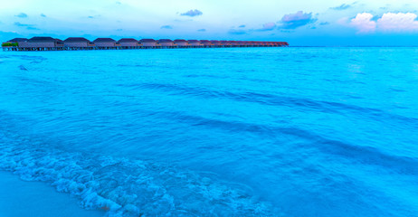 Wooden bridges leading to the huts on the shores of the tropical, warm sea. Maldives. Tourism concept.