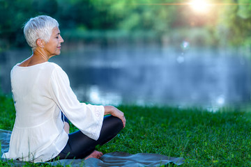 Fototapeta premium Senior woman meditating by the water