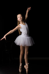 Naklejka premium Cute little girl in a tutu and pointe shoes is dancing in the studio on a black background.