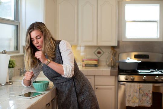 Coughing young woman in her kitchen, eating breakfast getting on her iPad 