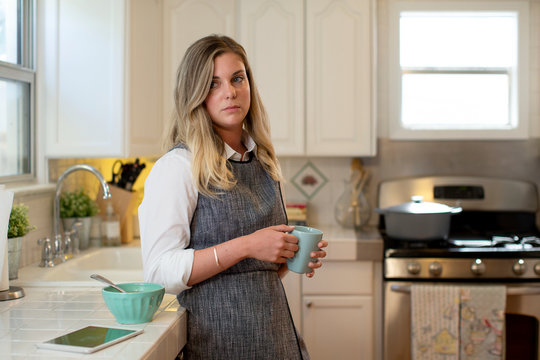 Young woman in her kitchen eating soup and drinking tea, looking off camera 