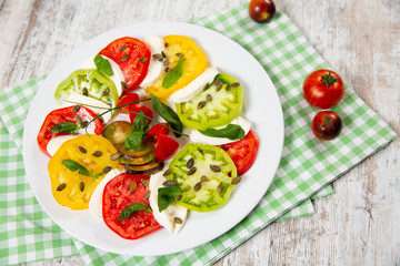Delicious caprese salad of yellow, green and red tomatoes with cheese and fresh basil