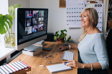 Smiling mature woman having video call via computer in the home office. Online team meeting video...