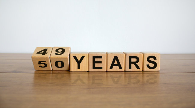 Turned cubes and changed the expression '49 years' to '50 years' or vice versa. Beautiful wooden table, white background. Business concept, copy space.