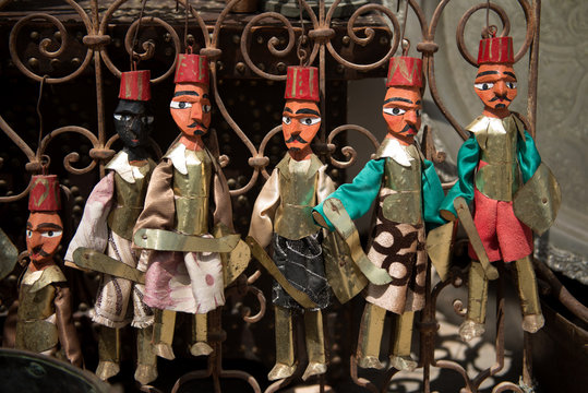 several handmade male toys made of wood in bright national costumes hang on a metal rod at a market in Tunisia