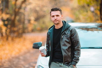 Young man drinking coffee with phone in autumn park outdoors