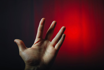 A male hand with an open palm and spread fingers shows a gesture against a red background with a dark vignette.