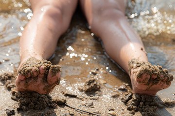 Child is sitting in in sand with feet completelly covered by sand