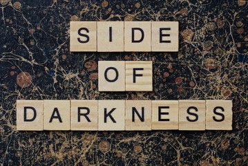 phrase side of darkness in small square wooden letters with black font on a brown background