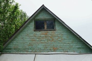 old green brick attic with a small one wooden window on a gray sky background