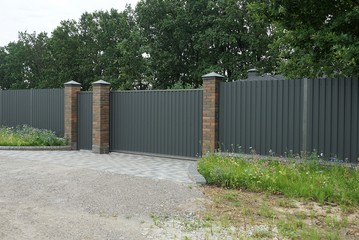 closed gray metal gates and a long iron fence on a rural street in green grass