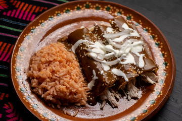 Mexican chicken enchiladas with mole sauce and rice on dark background