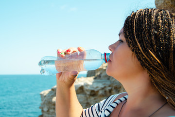 woman drinks water from a plastic bottle. Sits on a cliff at the top of a cliff. Against the backdrop of a beautiful landscape