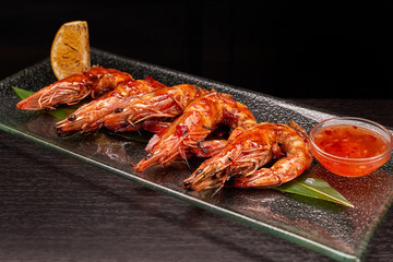 Fried king prawns on a bamboo leaf, on a transparent plate, with lemon and sauce