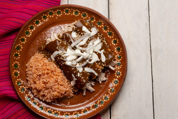 Mexican chicken enchiladas with mole sauce and rice on white background