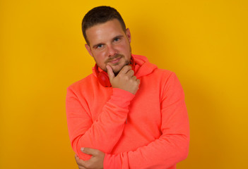 Portrait of thoughtful smiling man keeps hand under chin, looks directly at camera, listens something with interest, dressed casually, poses against gray wall. Youth concept.