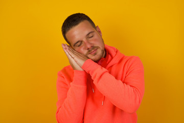 Relax and sleep time. Tired young handsome man with closed eyes leaning on palms as pillow pretending sleeping being exhausted seeing dreams standing against gray background. Sleeping gesture.