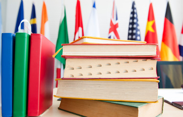 A pile of books on desk with calendar yearly planner over national flags cloth on poles background, Stacked of textbook with planner write meeting agenda for organizer to plan timetable against flags 