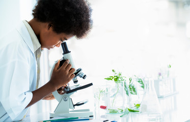 Afro american boy with curly hair as a researcher and biologist looking at a small green leaf...