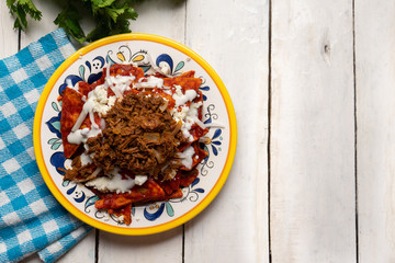 Mexican red chilaquiles with chilorio and cheese on white background