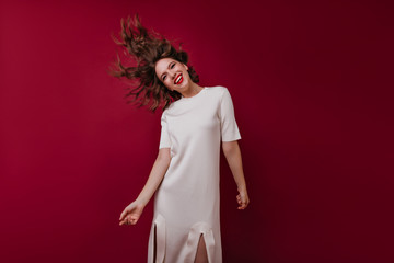 Fototapeta premium Debonair curly woman in white dress dancing on dark background. Indoor shot of refined european girl in good mood.