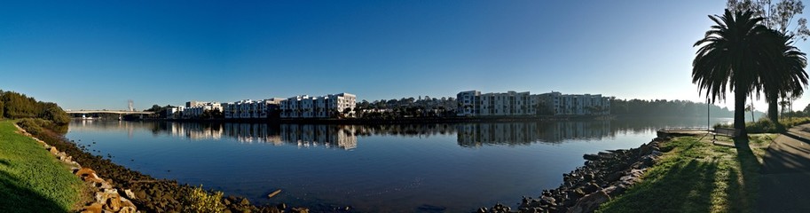 Beautiful panoramic view of a river with reflections of modern apartment buildings, deep blue sky and trees on water, Parramatta river, Wilson Park, Silverwater, Sydney, New South Wales, Australia
