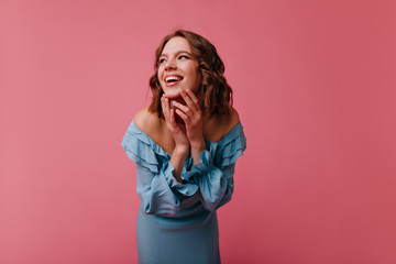 Wonderful caucasian lady in blue dress laughing in studio. Indoor photo of glad female model isolated on pink background.