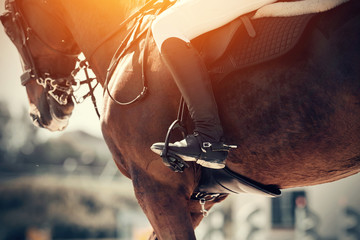 Equestrian sport. The leg of the rider in the stirrup, riding on a red horse.