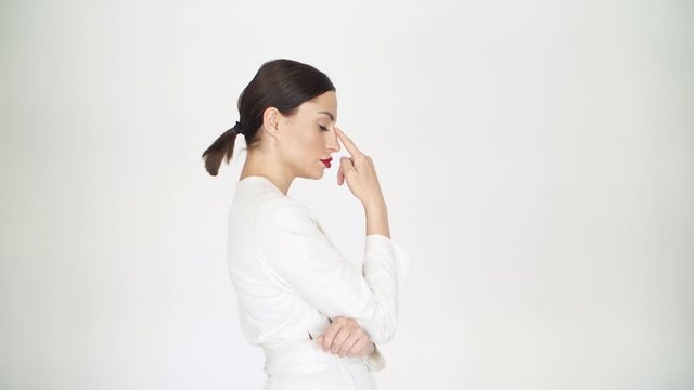 a girl in a white dress on a white background in profile to the camera points her fingers to the shape of her nose