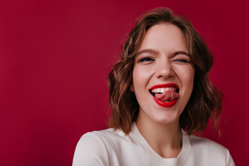 Close-up portrait of appealing girl posing with tongue out. Studio photo of jocund caucasian lady standing on dark background.
