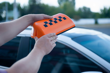 Orange sign of a taxi in the hands of a man on the background of a car. The driver went to work.