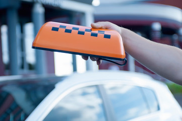Orange sign of a taxi in the hands of a man on the background of a car. The driver went to work.