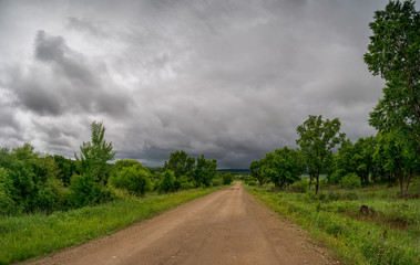 Landscape with a wide forest road and a sky with storm clouds