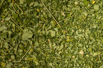 Macro of some green spices with a spoon and a pot on a wooden black surface  